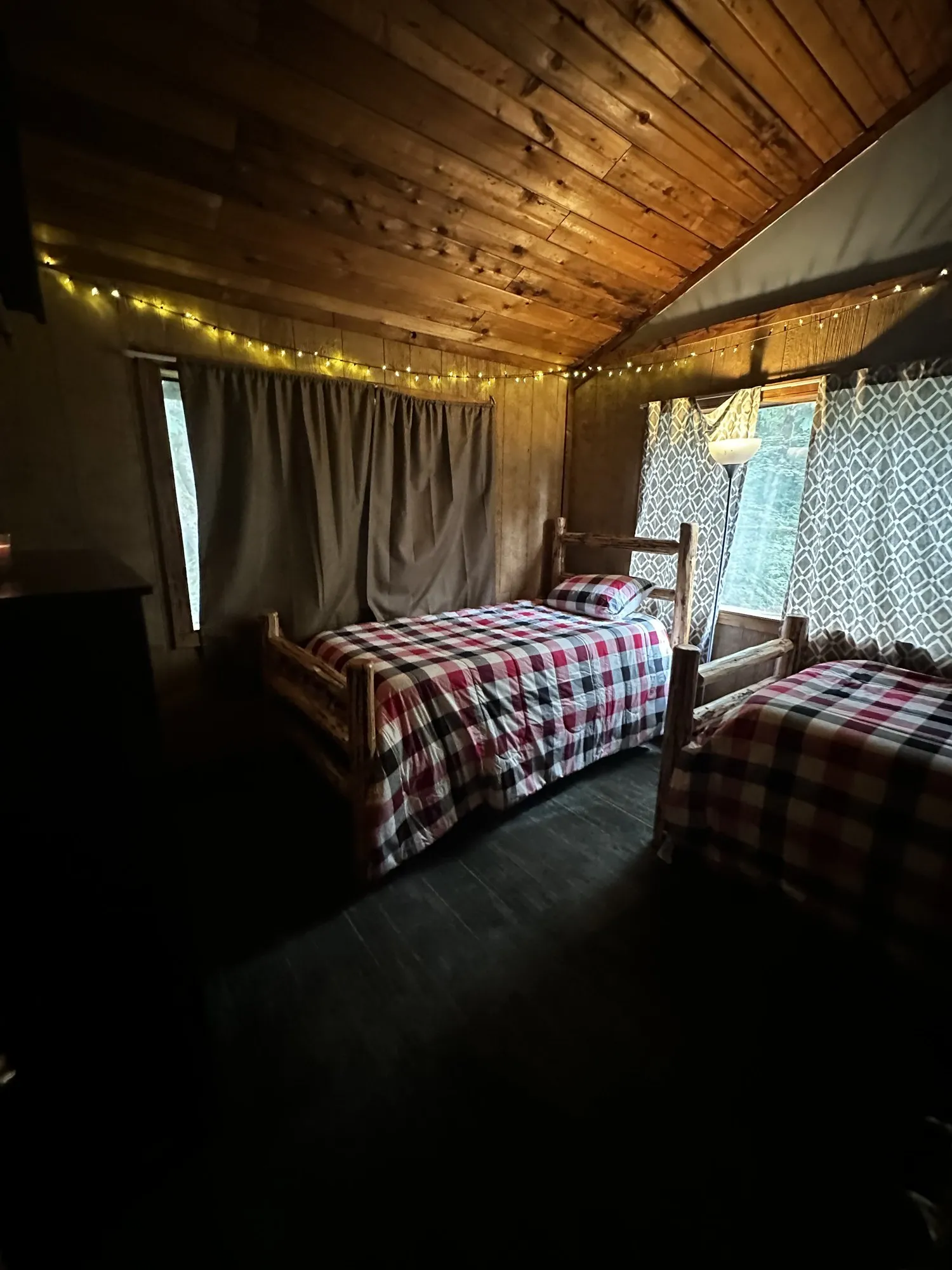 A residents' bedroom with two twin beds, plaid bedding, and warm string lights along the cedar ceiling